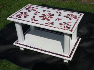 A rectangular white table with red mosaic patters around the edges and floral mosaic decoration in the middle.